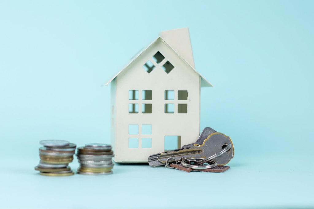 Miniature house model with coins and house keys on a light blue background, representing savings and protection related to US home insurance.