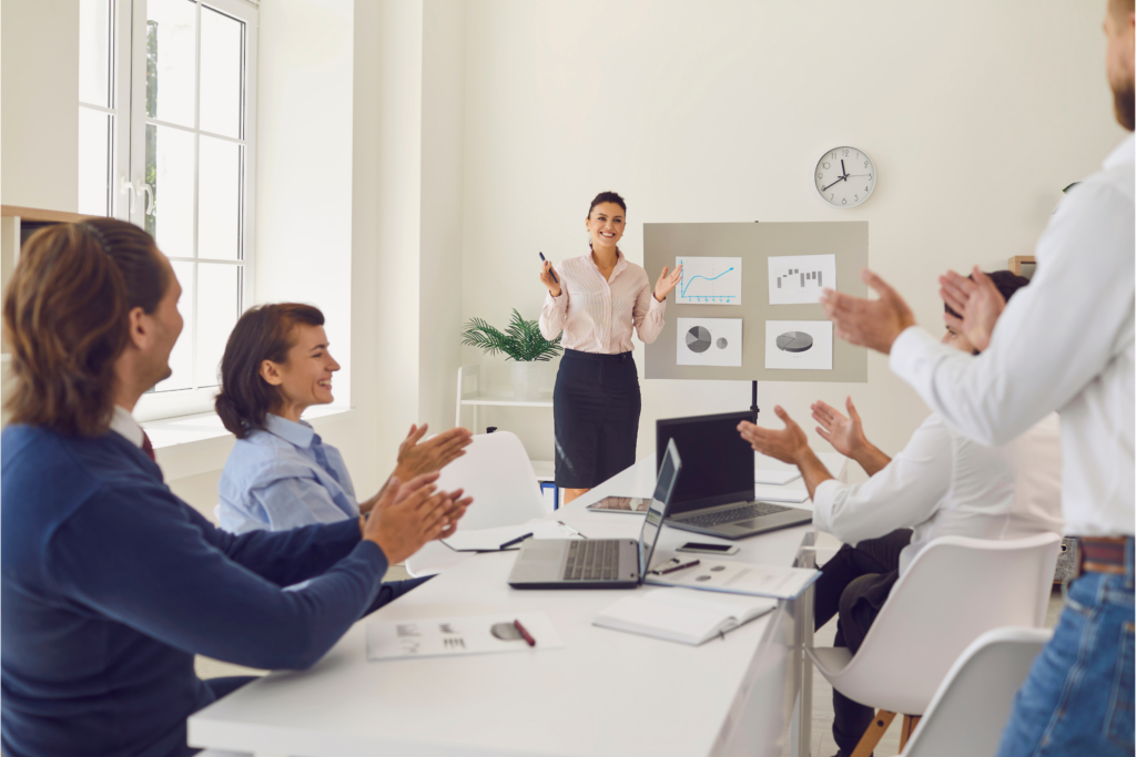 Professional business team applauding successful employee presenting data charts in bright modern office, illustrating the value of employee retention and avoiding the real cost of losing an employee