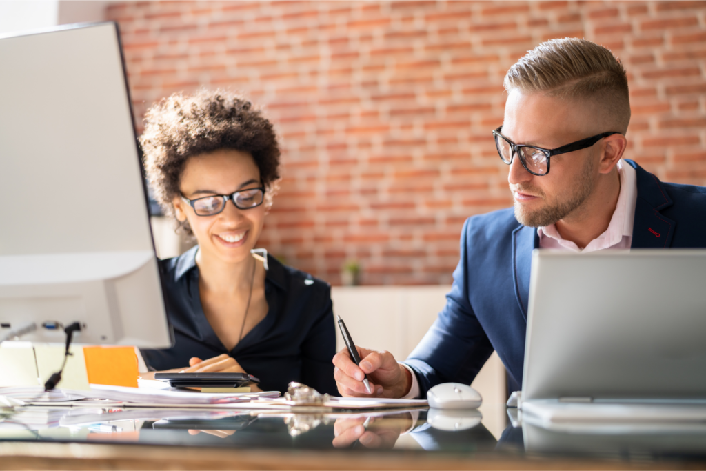 Two business professionals reviewing employee benefits compliance documents together at an office desk.